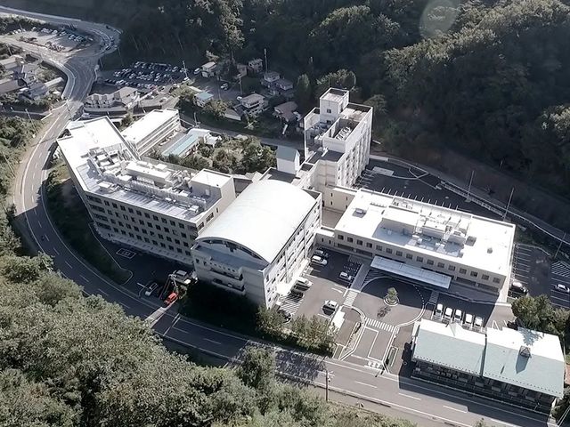 自然に囲まれた外観 外観   山あいに建つ大きな建物で、周囲の緑が印象的です。車寄せや駐車スペースも見え、働く場所の広さが伝わります。