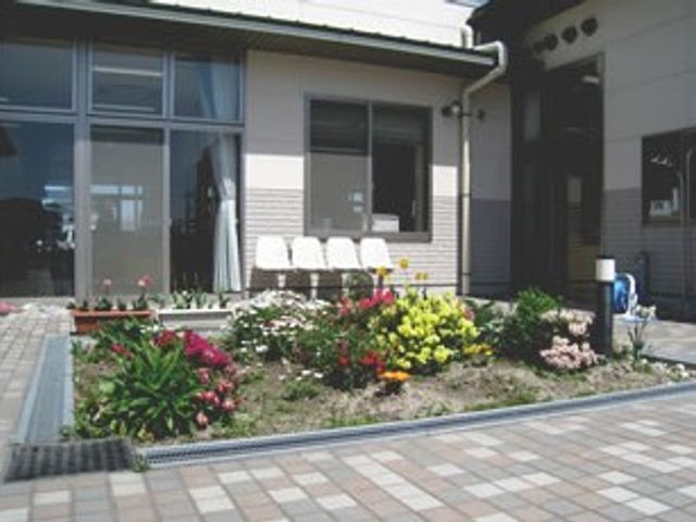 花壇のある玄関先の外観 外観   建物前に花壇が整えられ、明るい雰囲気の玄関まわりです。来訪者を迎えやすい、すっきりした出入り口になっています。
