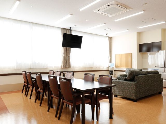 ゆったり過ごせる食堂 ダイニングルーム 広々としたダイニングルームです。テーブル周りにはいくつかの椅子が並び、壁際にはテレビとソファが設置されており、居心地の良い食事や憩いの場をご提供しています。