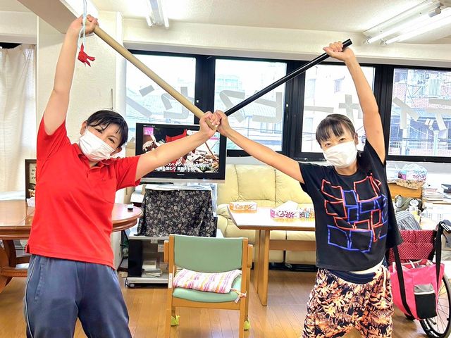 楽しい活動の時間 多目的室 明るい多目的室で、スタッフが元気に体を動かしています。楽しい雰囲気が感じられます。