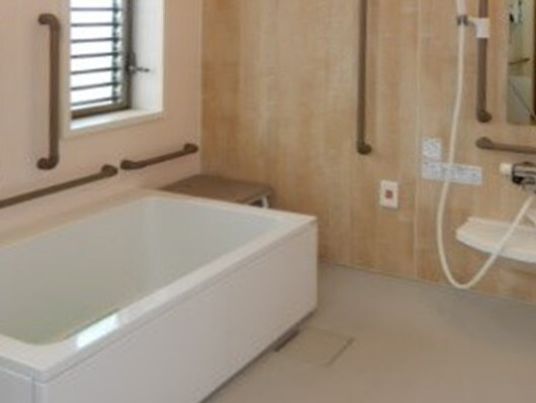 ブラウン系の手すりがたくさん設置された浴室。一人用の浴槽が設置され、ベンチも付いている。