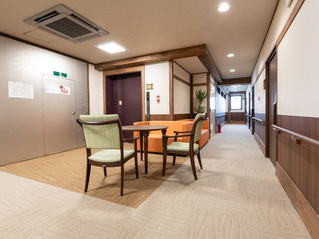 和風モダンな廊下 廊下 清潔感ある廊下には椅子やテーブルが置かれ、休憩や交流のスペースとして活用できます。木目調の装飾が温かみのある雰囲気を演出しています。