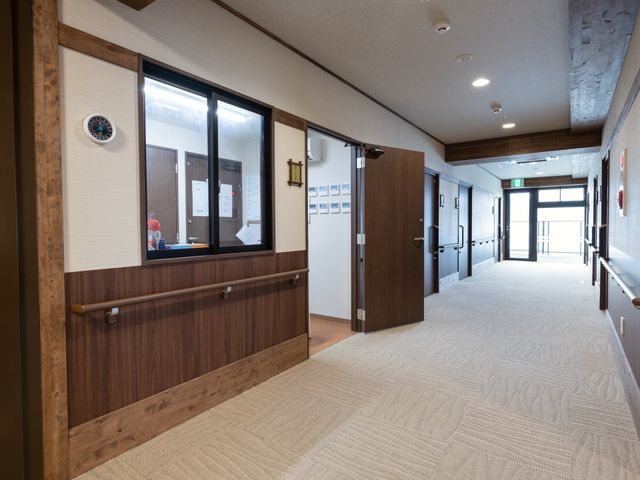 清潔感のある廊下 受付 落ち着いた色合いの廊下は、清潔で広々としており、安心して歩行ができる環境が整っています。手すりも設けられており、支えが必要な方も安心です。