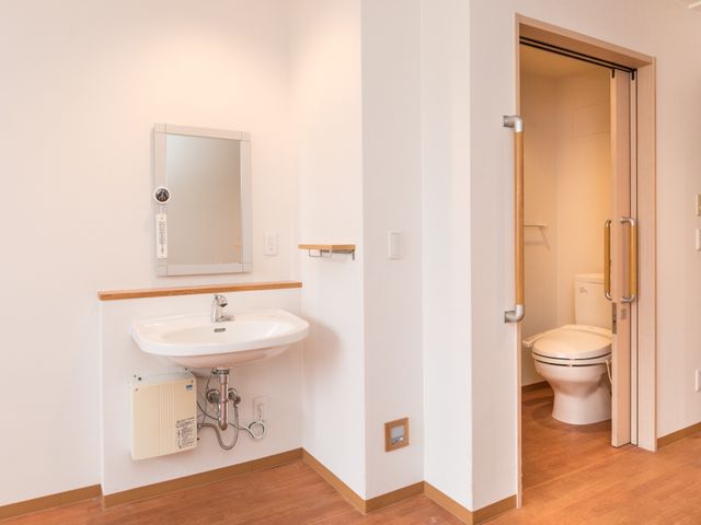 綺麗な洗面台とトイレ 居室 手すり付きのトイレは安全に配慮され、洗面台も清潔感のある設計です。快適にご利用いただける環境を整えています。
