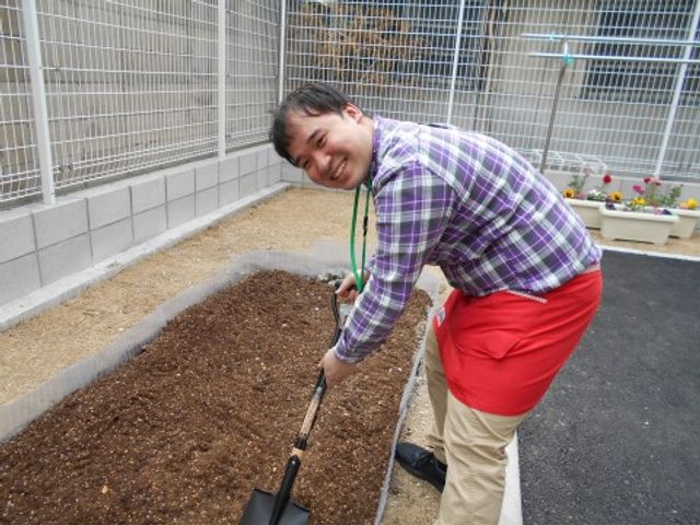 土を耕す男性 庭 笑顔で園芸作業を行うスタッフの姿が印象的です。手入れが行き届いたこの中庭で、利用者様と一緒に植物のお世話を楽しめます。