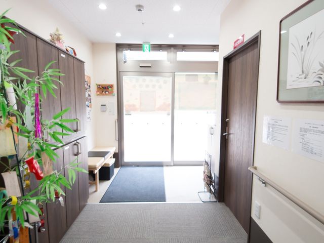 エントランスの明るい廊下 玄関 出入口は明るく、バリアフリー設計になっているため、どなたでも安心してご利用いただけます。壁掛けのアートや案内掲示が見られ、心地よい印象を受けます。