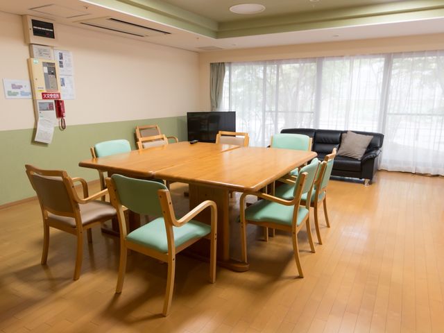 共有リビングの一角 リビングダイニング 温かみのあるリビングは、ゆったりとしたソファも完備しており、入居者様の憩いの場として最適です。窓の外の自然光が心地よい空間を演出しています。