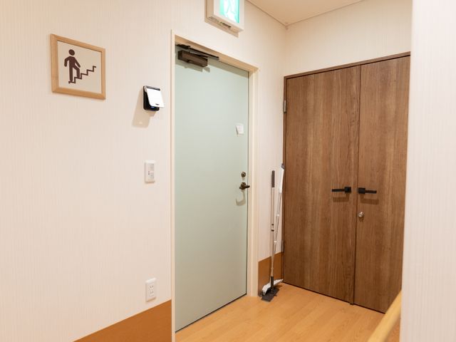 廊下にあるドアと階段の標識 階段 清潔感あふれる廊下は、開放感を与える木目調のドアで区切られています。利用者様の心地よい生活空間づくりに配慮した設計です。