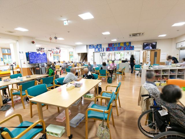 多様な椅子の共有ダイニング 食堂 明るく活気のあるダイニングルームで、利用者が食事や会話を楽しんでいます。スタッフが日々のサポートを提供し、快適な時間を過ごせるようにしています。