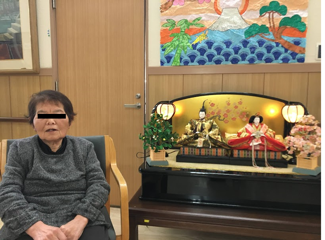 人形と座る女性の室内 多目的室 落ち着いた雰囲気の室内です。伝統的な人形が飾られており、心和む空間になっています。