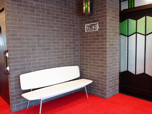 レストランの入り口前面は、トイレ付近から赤いカーペットのフロアが続いている。左側の壁際に白い椅子が置かれている。