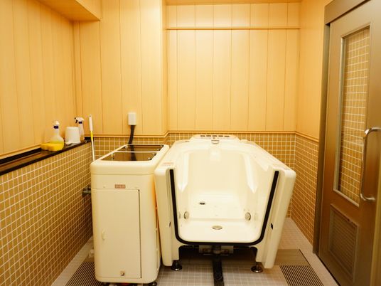 バスルームの床はベージュ、壁はオレンジ系のタイル張りである。無理のない姿勢のまま入浴できる介護浴槽が設置されている。
