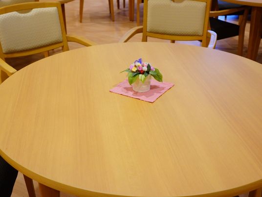 共有スペースに置かれているテーブルの材質は天然木で天板は円形である。ほぼ中央には小さな花の小物が飾られている。