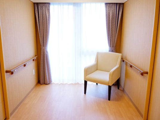 廊下の突き当たり部分には大きな窓があり、ダブルカーテンが掛けられている。ボックスタイプの白い椅子が1脚置かれている。