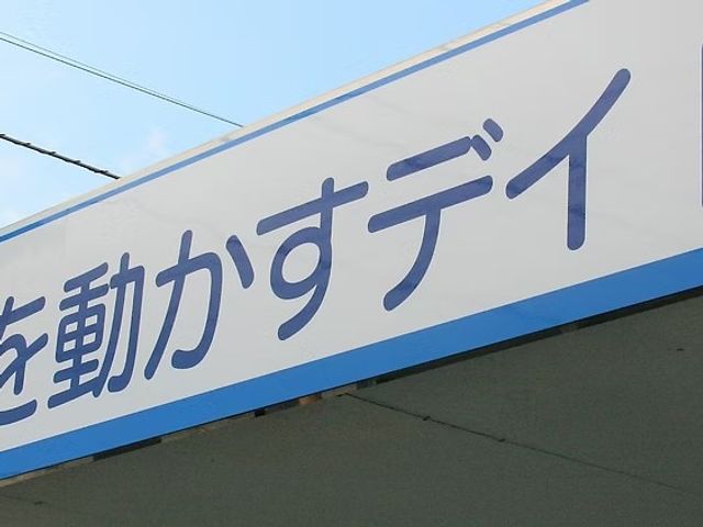 看板の一部 看板   青い縁取りのある看板に、施設名の文字が大きく表示されています。明るい空の下で、建物の印象を伝えています。