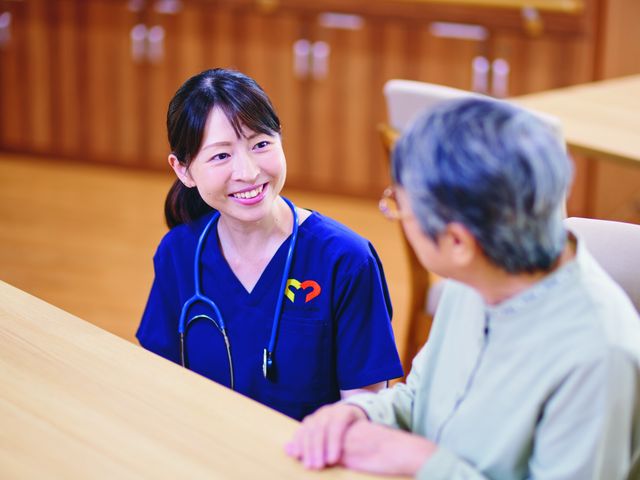スタッフと利用者の交流 ダイニングルーム スタッフが利用者と親しげに会話しています。温かいコミュニケーションを大切にする施設です。