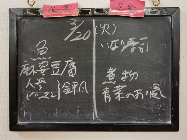 黒板に書かれたメニュー表示 献立 毎日の献立が手書きで示され、利用者の食事時間も明記されており、日々の生活に彩りを与えています。