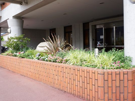 両脇の支柱から一歩前に出たような横に長いレンガの花壇は多くの草を生やしており、その中には白やピンク色の花々が咲いている。
