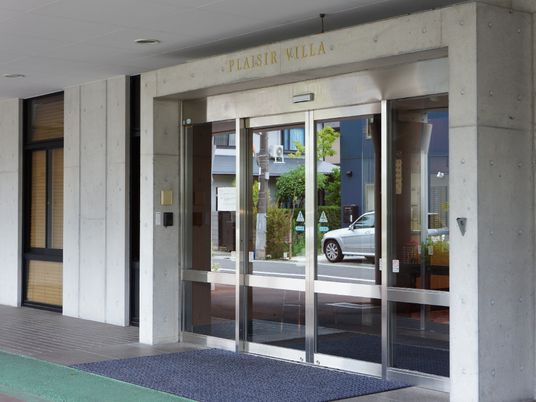 コンクリートで囲まれた4つの大きなガラス窓は内側の二つが自動ドアとなっている。ドアの下には玄関マットが敷かれている。