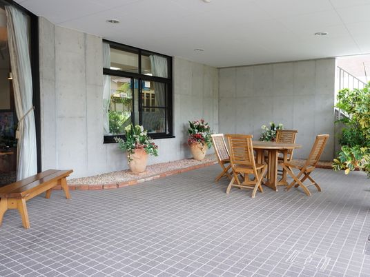 白い天井の下には木製の丸い机があり、その机を囲うように4つの木製でできた椅子が置かれている。建物側には花をいけられた2つの壺がある。