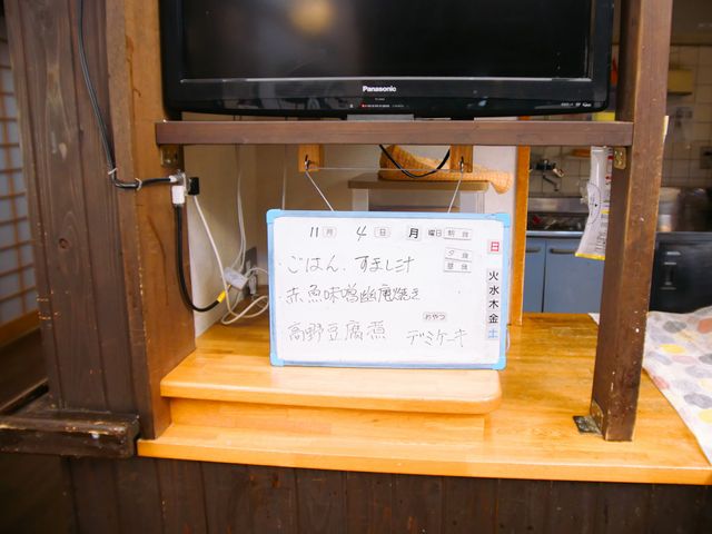 日程を示す掲示物とテレビ 掲示物 明日のイベント情報が掲示された木造の棚です。居心地の良い空間で日々の生活に彩りを。