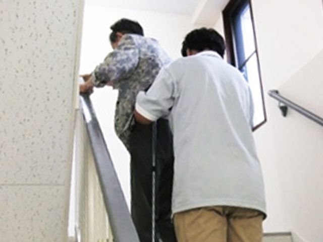 介助中の階段 廊下 介護スタッフが利用者をサポートしながら階段を上る様子です。安全に配慮された環境です。