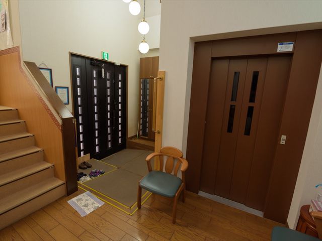 玄関付近の廊下と階段 玄関 エントランス付近が広々としており、段差も少なく利用者の安全に配慮された設計です。居心地の良い椅子も用意され、待ち時間も快適に過ごせます。