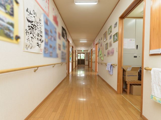 温もりある木の廊下 通路 壁には色とりどりの作品が飾られ、廊下は歩きやすく手すりが整備されているため、日々の移動も快適です。