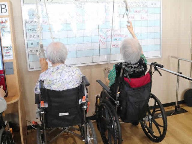 居室で過ごす人々 掲示物 ホワイトボードを前に積極的に参加する入居者の様子です。多くの活動が行われ、コミュニケーションの場が提供されています。