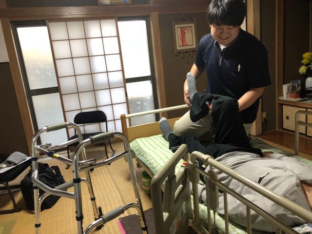 介護士が入居者をサポートする居室 居室 自然光が差し込む落ち着いた空間で、介護士が温かくサポートしています。木のぬくもりが感じられます。