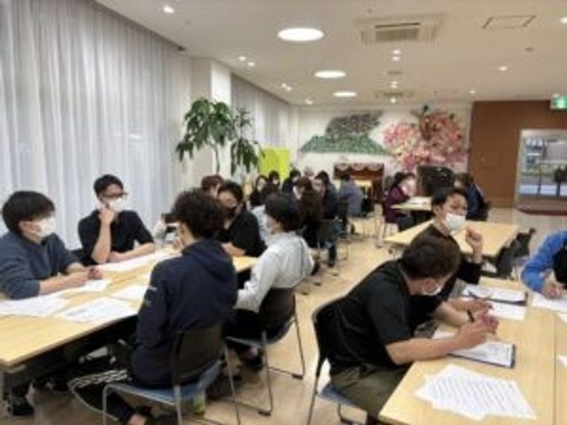 会議中の多目的室 多目的室   明るい広い空間で、複数の方が机を囲んで打ち合わせをしています。就業前に現場の雰囲気を知りたい方にも参考になります。
