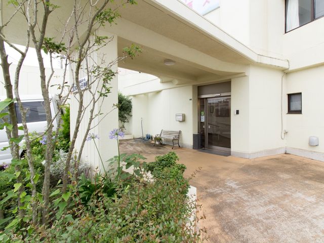 緑豊かな施設のエントランス 玄関 広々としたエントランスは、訪れる人々を温かく迎えます。植栽も手入れされ、明るい雰囲気が漂います。