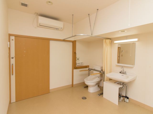 洋室のトイレと洗面台 洗面化粧台 ゆとりある広さの洋室で、車椅子の方も使いやすい工夫がされたトイレと洗面台が完備されています。快適な個室での生活をご支援します。