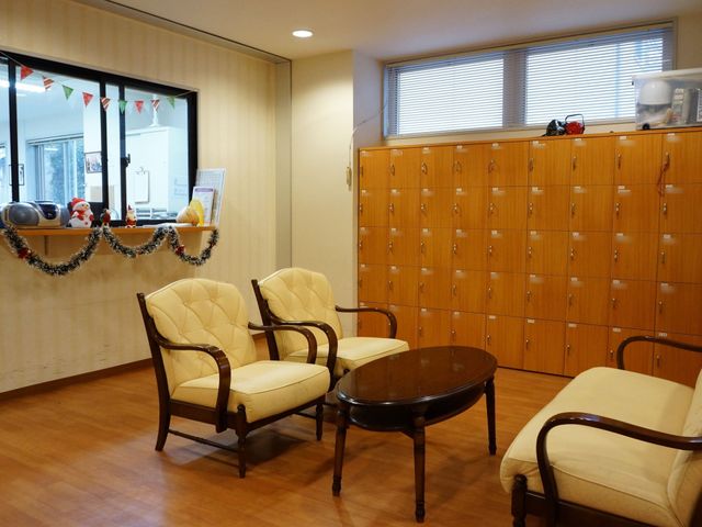 居心地の良い休憩室 玄関 温かみのある木製の椅子とテーブルが配置され、リラックスできる空間となっています。ロッカーも完備され、利用者のプライバシーにも配慮されています。