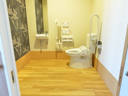 バリアフリーの広いトイレは、一部の壁に花柄のクロスを採用したスタイリッシュな空間となっている。手すりと呼出ボタン、手洗い場も設置されている。