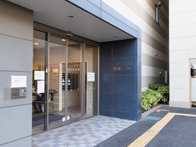 施設入口とスタッフ 玄関 この入口は自動ドアで、出入りに便利です。スタッフの方が笑顔で迎えてくれる様子が見受けられます。