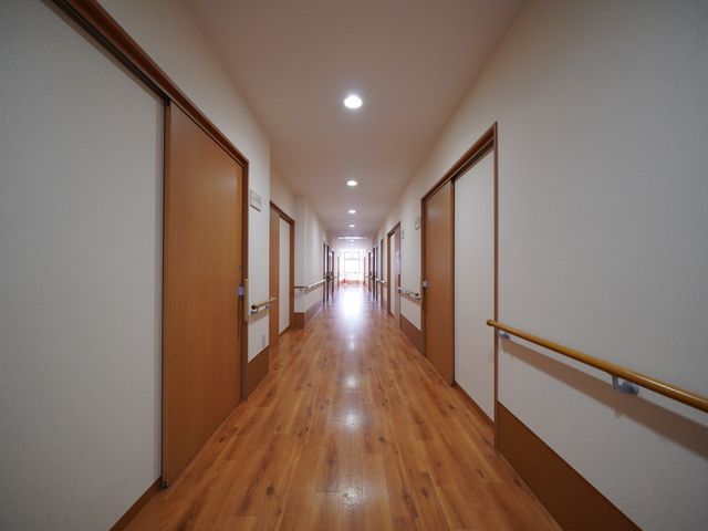 明るい木目調の廊下 通路 清潔感のあふれる廊下は、明るい木目調で統一されており、安全に配慮した手すりが設置されています。ゆったりとした空間が広がり、快適な移動を支援します。