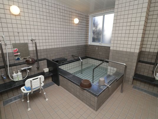 施設の写真 大人数で利用できる大浴場があり、窓がついている。浴槽の縁に洗面器や手桶がある。洗い場が２か所にある。