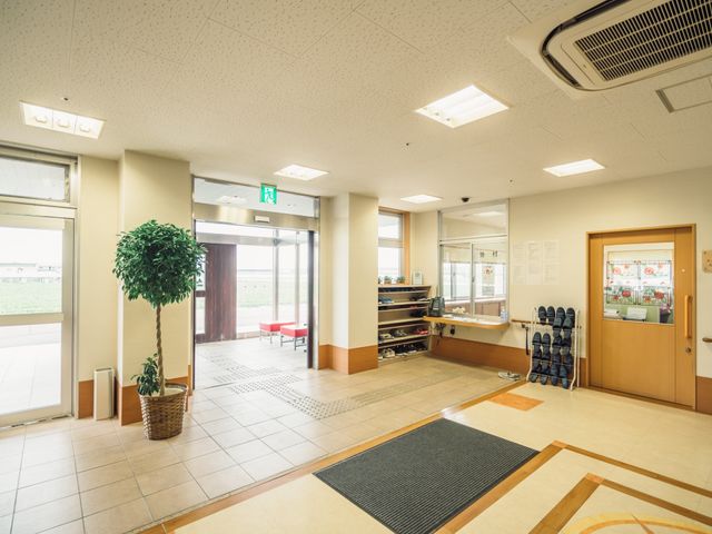 明るいエントランスの風景 玄関 ゆったりとした出入口は明るく開放感があります。笑顔で迎える受付も見え、訪れる人々を暖かく迎え入れてくれます。