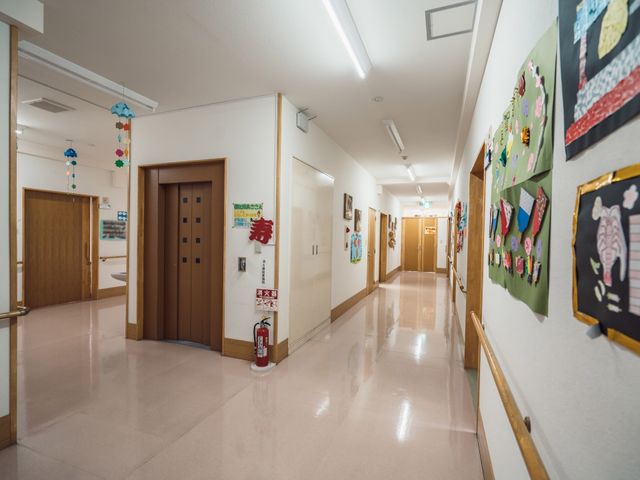 廊下に掲示物と装飾 通路 明るく清潔な廊下が整備され、壁には季節感ある工作物が飾られています。利用者の創造性を育む工夫が見られます。