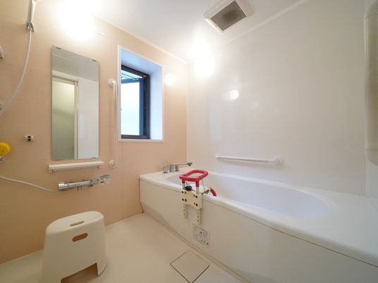 浴室に腰かけが置かれている。浴槽のふちには可動式の手すりが、壁面には固定式の横長の手すりが設置されている。