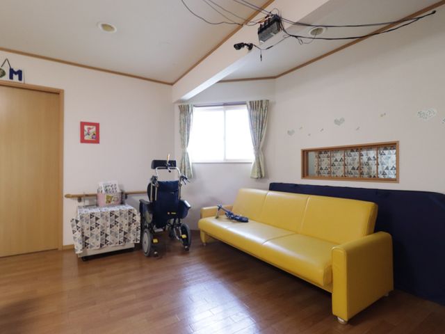 ゆとりある居室の一角 共有スペース 明るくアットホームな雰囲気の居室です。ソファや車椅子が配置されており、ゆったりとくつろげるスペースが整っています。