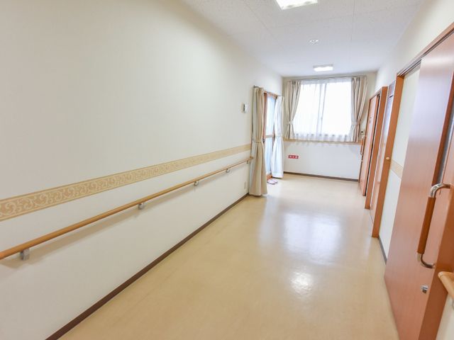 明るい廊下の一角 施設廊下 手すりが付いた広々とした廊下は、安全で快適な移動をお手伝いします。窓からは自然光が差し込み、温かな雰囲気を醸し出しています。