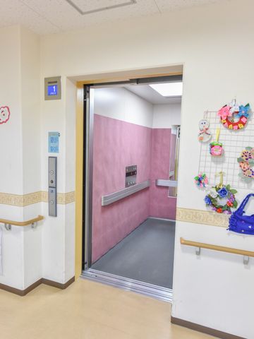 エレベーター前の廊下 エレベーター内 広々としたエレベーター前の空間です。壁に飾られた手作りの装飾品が、暖かみのある雰囲気を演出しています。