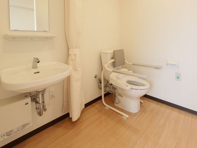 バリアフリー対応の洗面所 トイレ 手すり付きで安全に配慮された清潔なトイレ空間です。利用者の自立支援を考慮した設計になっています。