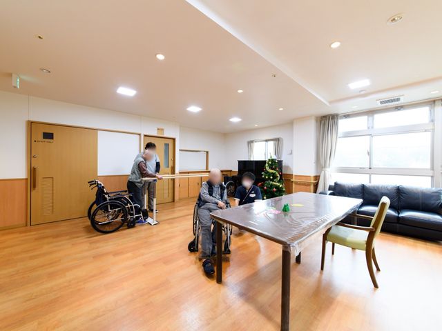 明るい共有リビング空間 リビング 居心地の良いリビングで、スタッフが入居者様と向き合いながらサポートしています。周囲は大きな窓で光があふれ、家庭的な雰囲気が広がっています。