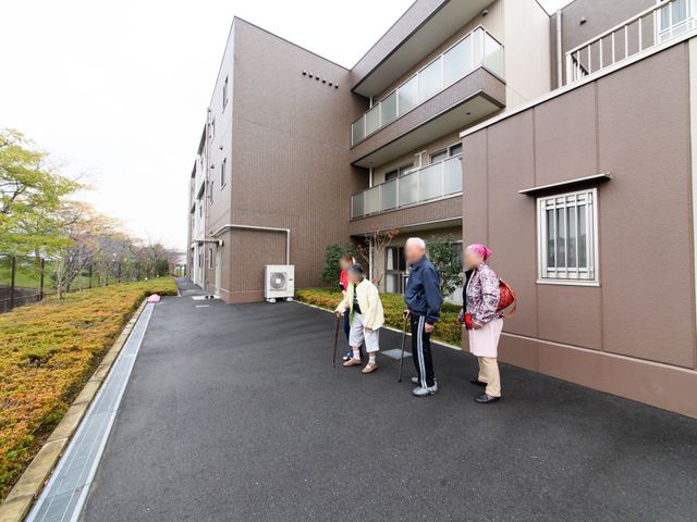 清潔で落ち着いた外観 外観 広々としたアプローチがあり、四季折々の自然を感じながら散歩が楽しめる外観です。手すり沿いに歩く人々の姿が和やかな雰囲気を演出しています。