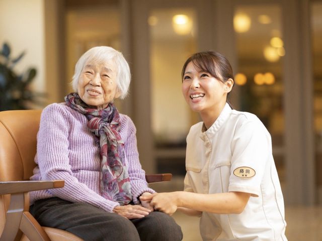 笑顔の職員と利用者 リビング 職員と利用者が和やかに交流しています。温かい雰囲気の中で、心地よい時間を共有できます。