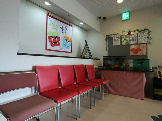 施設の写真 金魚が泳ぐ水槽や、季節のイベントを表現した絵などがある休憩コーナーが設けられている。赤い座面の椅子が４つ置かれている。