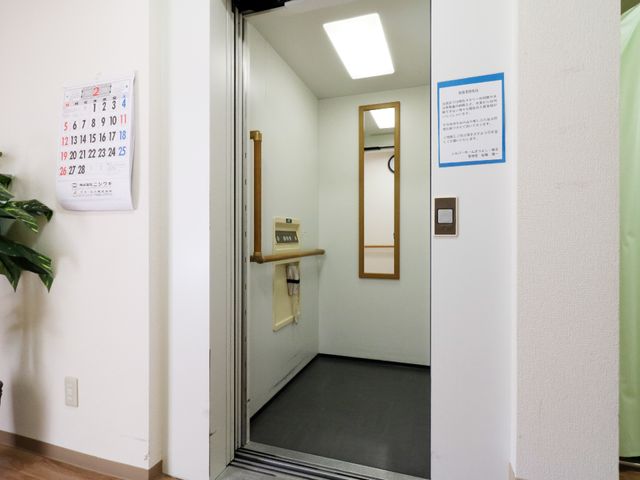 扉付きのシンプルな廊下 エレベーター この通路は壁面に案内板があり、安心して利用できる設計となっています。また、非常用の呼び出しボタンも設置されております。